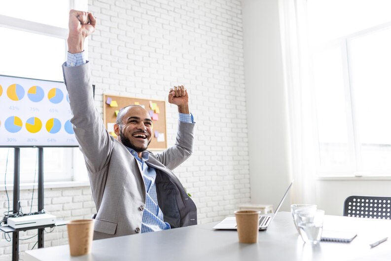 A happy young professional celebrating career success in an office setting.