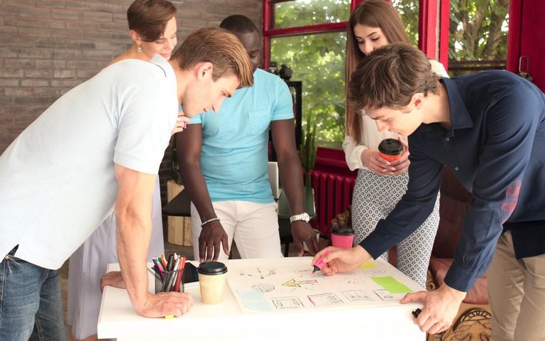A diverse group of young professionals collaborating around a table, discussing plans and taking notes, representing teamwork in youth work.